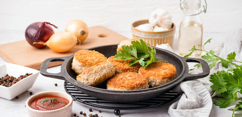 Frying pan with tasty meat cutlets and sauce on white background