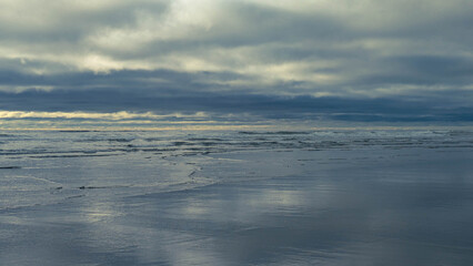 Side view from a wet beach with small waves rolling in, out westward towards the pacific ocean, under a majestic and complicated cloud-scape on a summer day