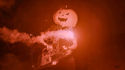 Halloween human pumpkin or Jack o lantern costume on a dark night with lots of smoke, a chainsaw,...