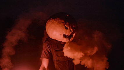 Halloween human pumpkin or Jack o lantern costume on a dark night with lots of smoke, a chainsaw,...