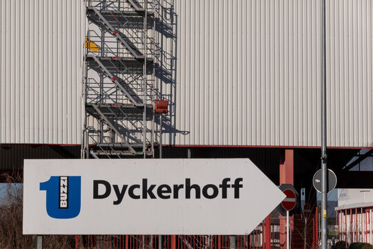 Neuwied, Germany - January 28, 2024: Buzzi Dyckerhoff company sign pointing right, showing the industrial factory building with corrugated metal facade and visible scaffolding under a clear sky