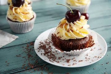 Plate with sweet cherry cupcake on blue wooden background