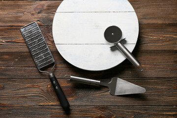 Set of kitchen utensils with stainless steel pizza cutter and board on wooden background