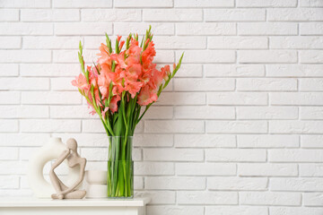 Vase with gladiolus flowers and statuette on commode near white brick wall