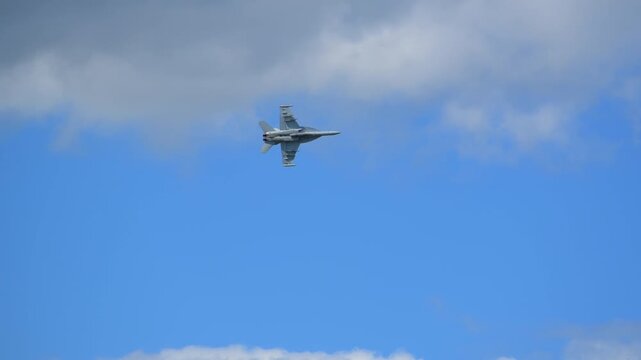 Close-up view of F-18 fighter jet at full power maneuver against a cloudy sky during an airshow, showcasing military strength, speed, and precision.
