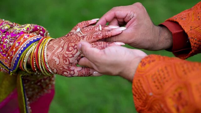 Groom is putting on the wedding ring on Traditional henna painted bridal hand. Elements of Hindu bright wedding clothes. 