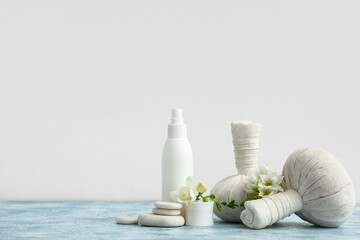 Cosmetic products, massage bags, spa stones and flowers on color table against light background