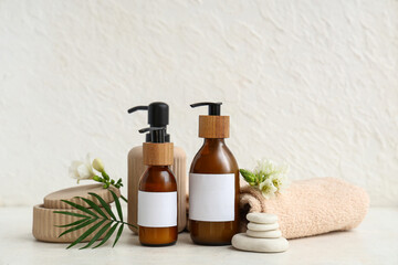 Bottles of cosmetic products, spa stones, towel and flowers on light background