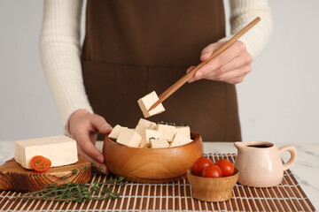 Woman with bowl of tasty tofu cheese on table