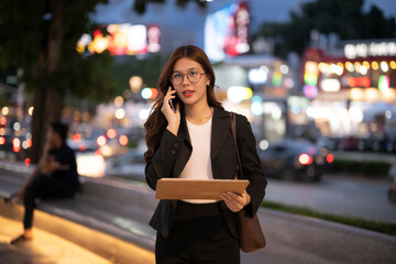 Asian businesswoman talking on phone walking city street at night