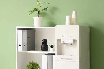 Interior of stylish office with modern water cooler, houseplants and shelving unit