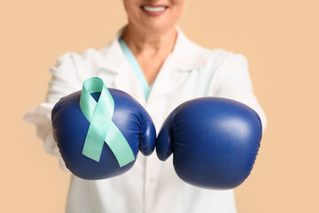 Mature female doctor with boxing gloves and teal ribbon on beige background, closeup. Cervical Health Awareness Month