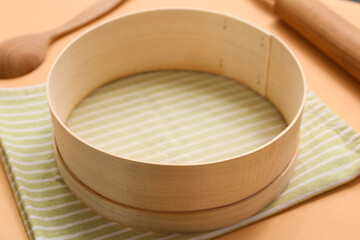 Wooden sieve, napkin, spoon and rolling pin on color background, closeup