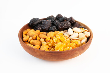 A close up of a bowl holds almonds, pistachios, raisins, and dates on a white background.
