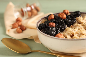 Bowl of tasty oatmeal with prunes and hazelnuts, closeup