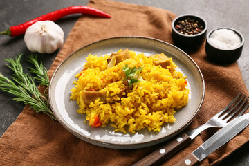 Plate with tasty pilaf and different spices on black background