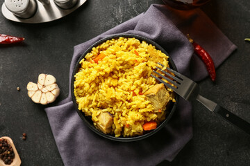 Bowl of tasty pilaf with chili peppers and garlic on black background