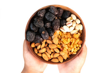 A person's hands hold a wooden bowl filled with various types of nuts and dried fruit.
