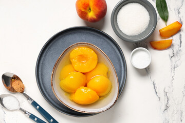 Composition with bowl of tasty canned peaches and sugar on light background