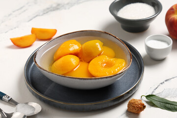 Bowls of tasty canned peaches and sugar on light background