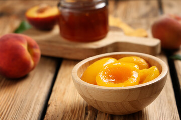 Bowl with tasty canned peaches and jar of jam on wooden table