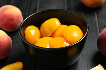 Bowl of tasty canned peaches and fresh fruits on dark wooden table