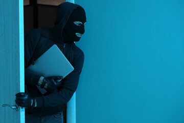 Male thief with stolen laptop walking through door at night