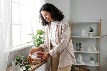 Young African-American woman with air humidifier and essential oils on commode in bedroom