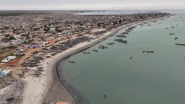 Wide aerial panorama of Joal Fadiouth, Senegal, capturing the coastline, sandy beach, and fishing boats scattered along the Atlantic Ocean shore