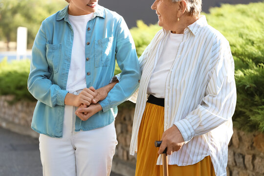Fototapeta Senior woman with stick and caregiver holding hands on street