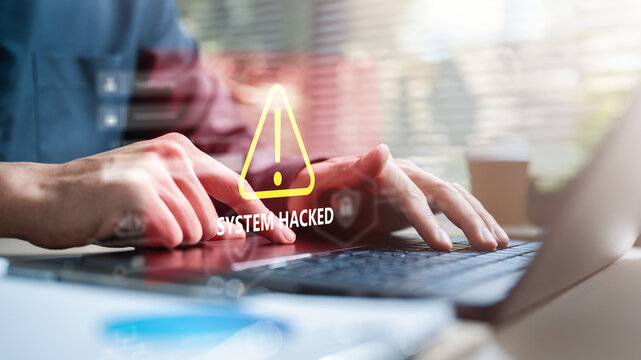Hands typing on laptop with system hacked warning sign, representing cyber attack, data breach, and online security risk.