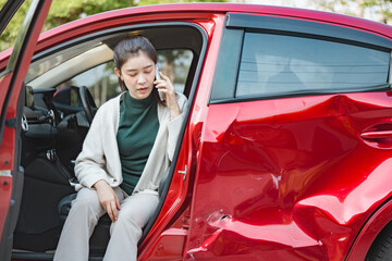 Distressed woman sitting in a red car with visible side damage after an accident, calling on mobile...