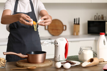 Woman with mixer separating white from yolk of egg at table in kitchen