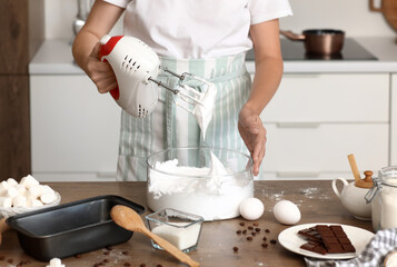 Woman whipping egg albumen with mixer at table in kitchen