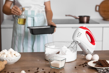 Mixer with whipped egg albumen on table against woman baking in kitchen, closeup