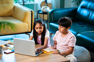 Indian Asian siblings kids learning with laptop, books, and notepad while studying together at home