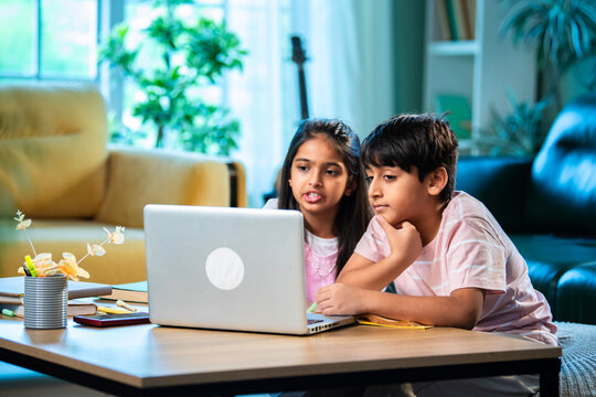 Indian Asian siblings kids learning with laptop, books, and notepad while studying together at home - Powered by Adobe