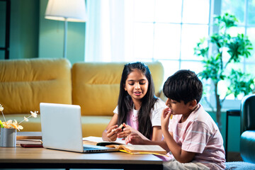 Obraz premium Indian Asian siblings kids learning with laptop, books, and notepad while studying together at home