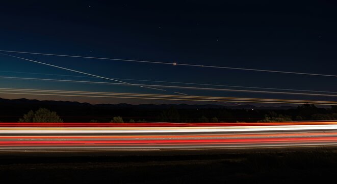 Nighttime highway with light trails and airplane contrails