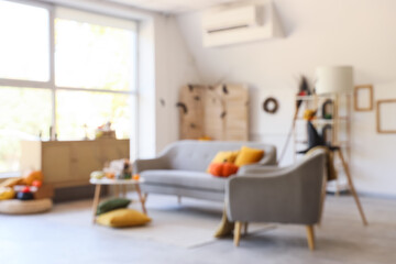 Blurred view of light living room decorated for Halloween with grey sofa, armchair and table