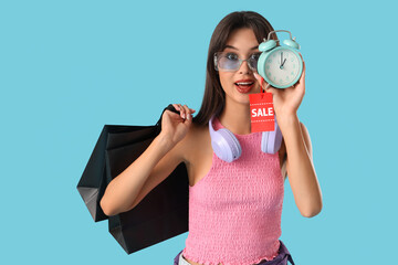 Obraz premium Young woman with shopping bags and alarm clock on blue background. Cyber Monday