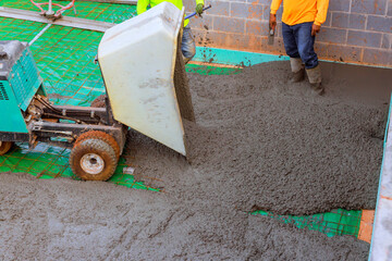 Contractor using concrete wheelbarrow machine pouring fresh concrete to create foundation in new...