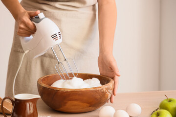 Woman whipping egg albumen with mixer in kitchen, closeup