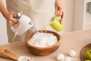 Woman whipping egg albumen with mixer in kitchen, closeup