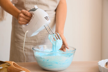 Woman whipping blue egg albumen with mixer in kitchen, closeup