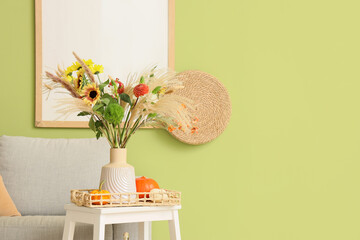 Vase with autumn flowers and pumpkins on stool in living room