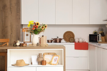 Interior of light kitchen with table, counters and autumn flowers in vase