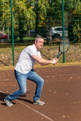 Man in jeans and t-shirt playing tennis on outdoors court