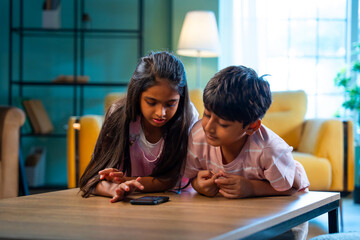 Indian Asian siblings kids using smartphones to play games while enjoying leisure time at home
