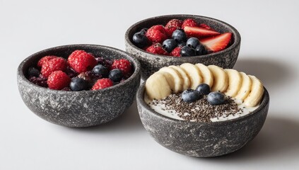 Three bowls of vibrant fruit and yogurt parfaits.  Each bowl displays a unique combination of fresh berries, sliced banana, and a sprinkle of seeds. The bowls are dark gray, with a textured surface